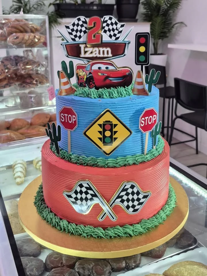 Tarta infantil de dos pisos inspirada en coches de carreras, decorada en azul, rojo y verde