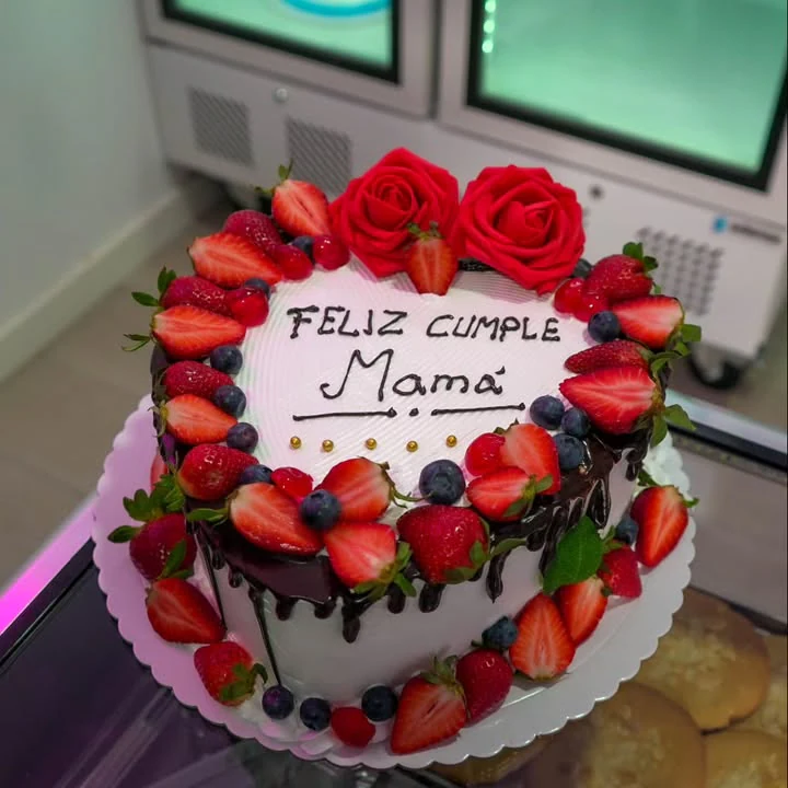 Tarta redonda con cobertura clara, chocolate, fresas, arándanos, frambuesas y rosas rojas