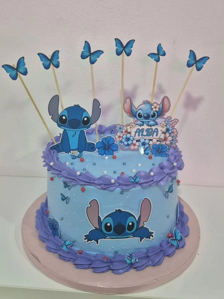 Tarta infantil azul y lavanda con personajes, flores, mariposas y perlas de azúcar