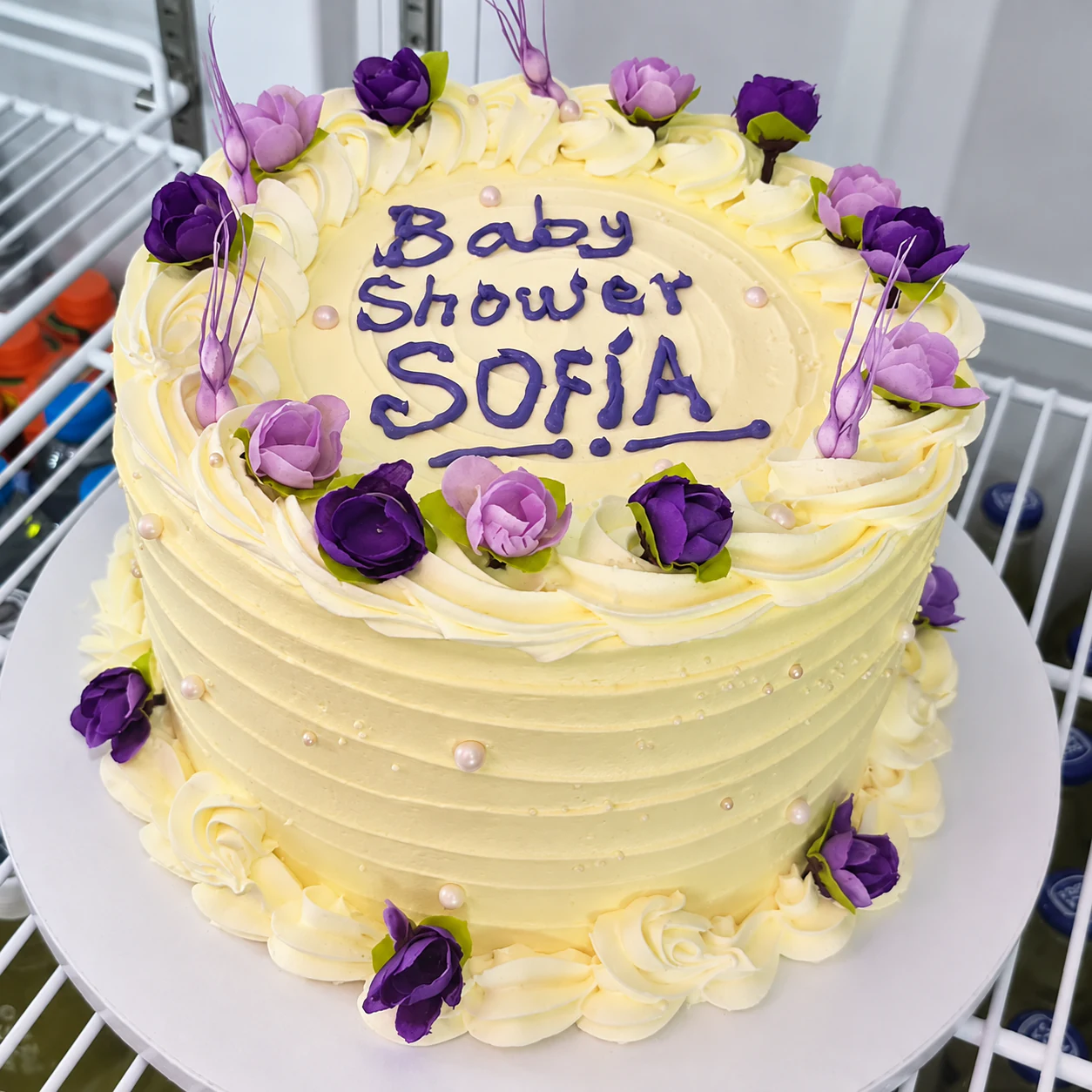 Tarta de crema clara con rosas lilas y violetas preparada para un baby shower