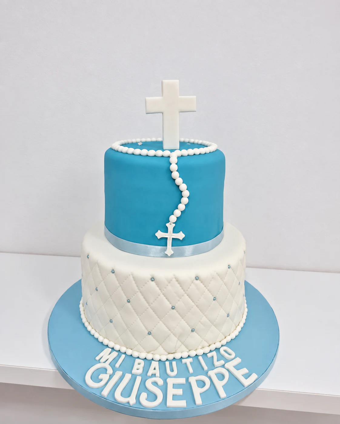 Tarta de bautizo de dos pisos en blanco y azul celeste con cruces y rosario
